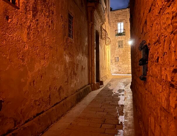 An old narrow street and doors, lit by lamps at night