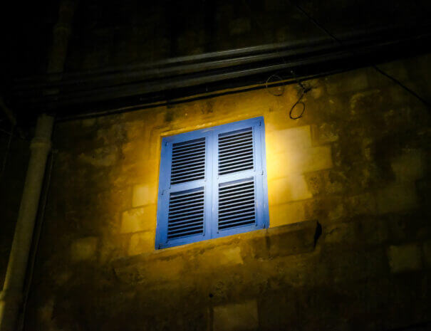 A window with closed blue shutters, lit up at night